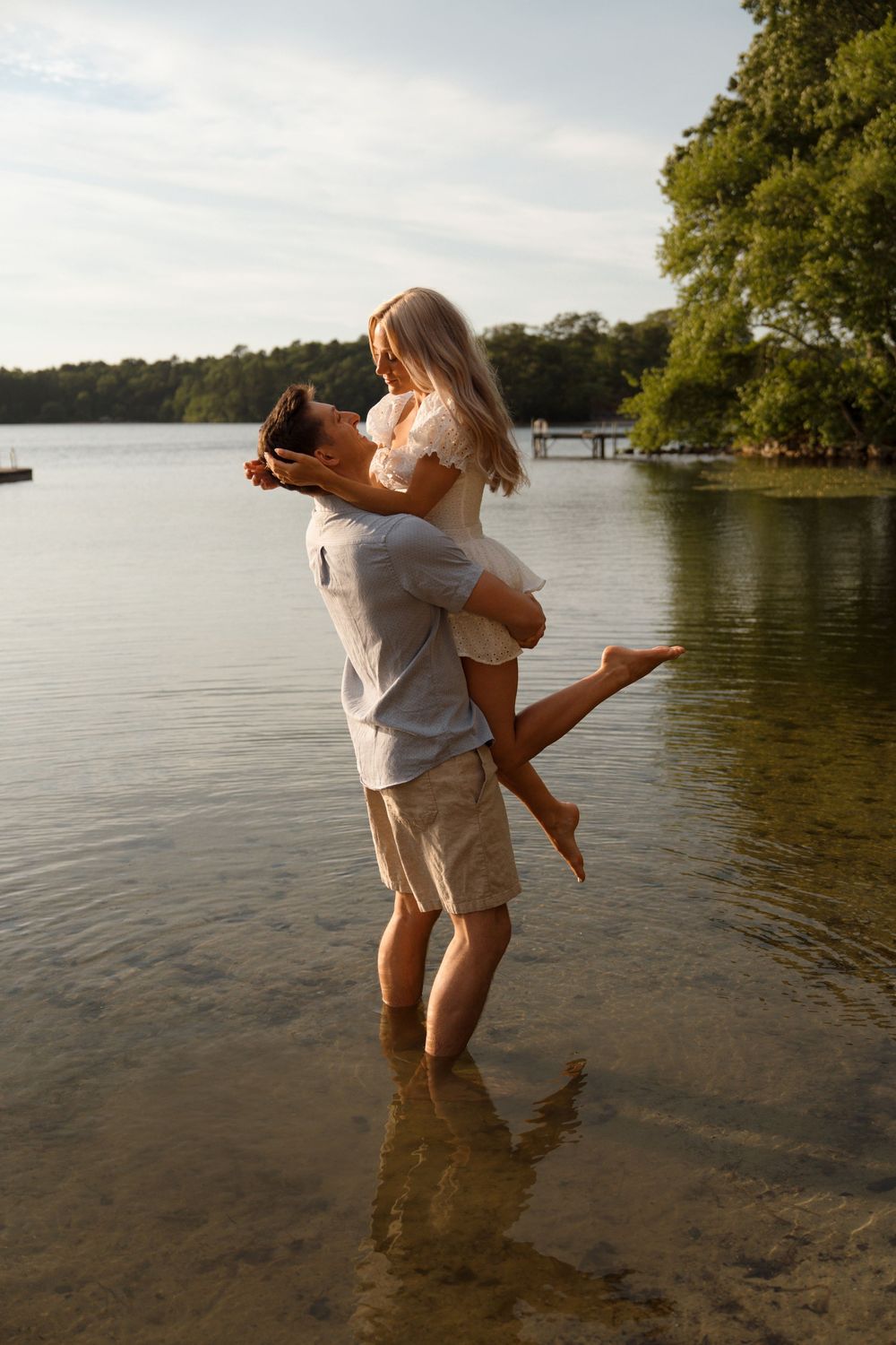 A romantic moment captured at a lake with two people embracing in shallow water during sunset.