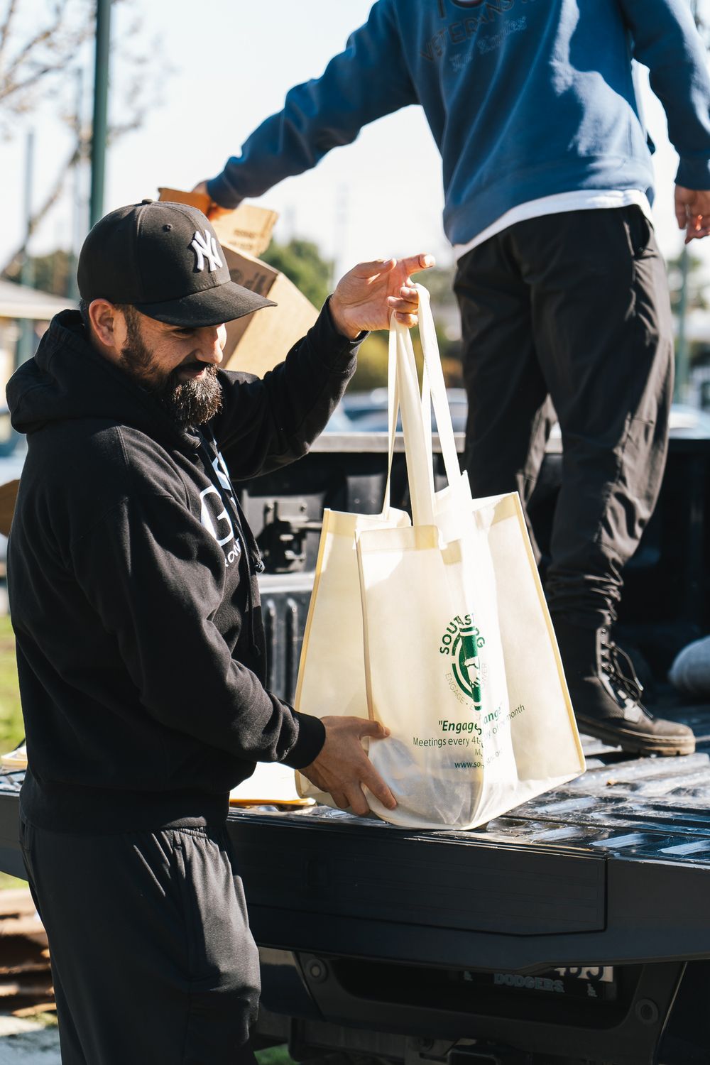 People in dark jackets distribute items from tables at an outdoor community event.