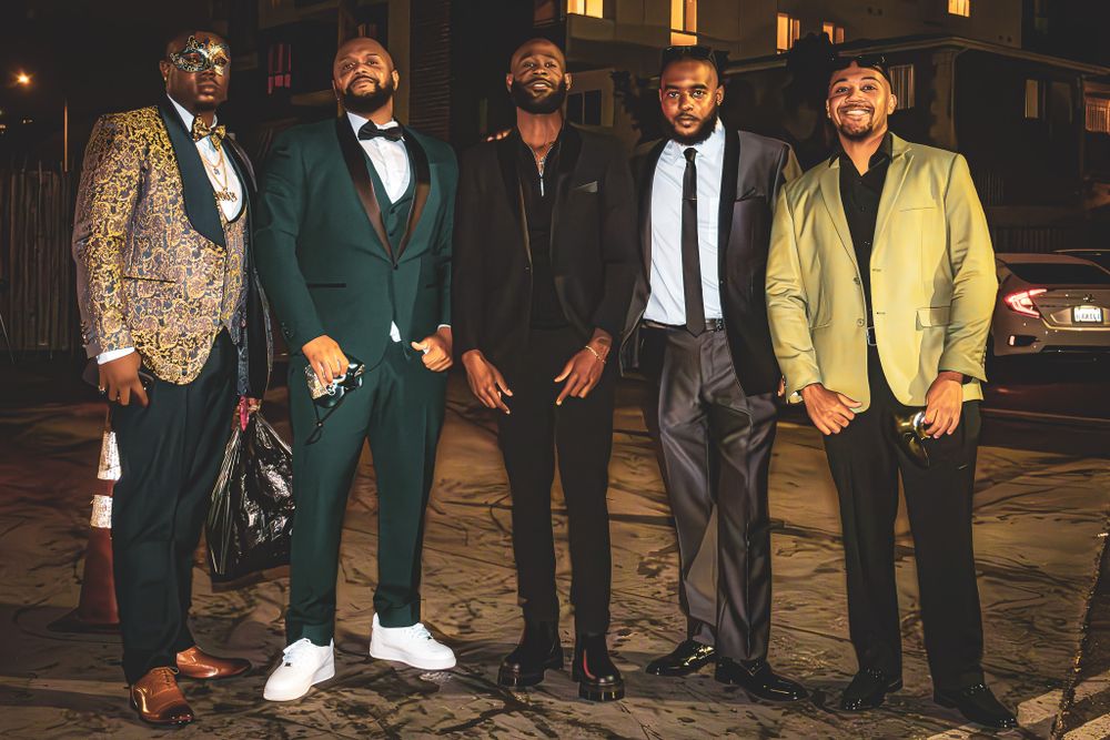 Five men in formal attire pose together at night, wearing stylish suits in various colors.