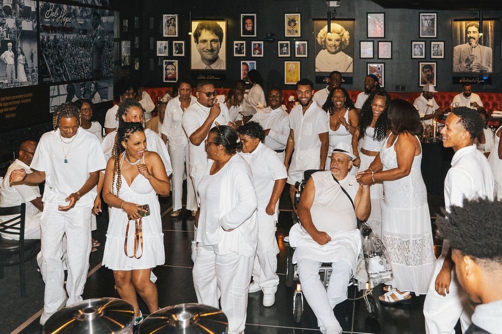 Celebration scene with groups of people in white attire mingling in a venue with wall art.