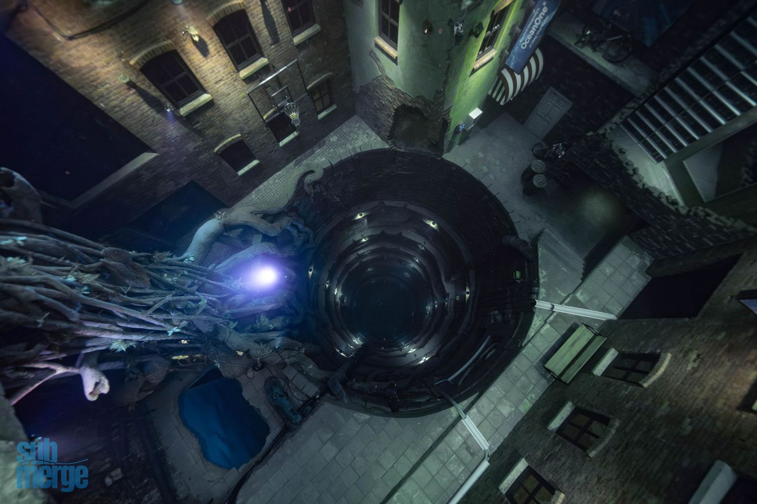 A high angle view of a dark industrial chamber with glowing blue lights and mechanical components in the shadows.