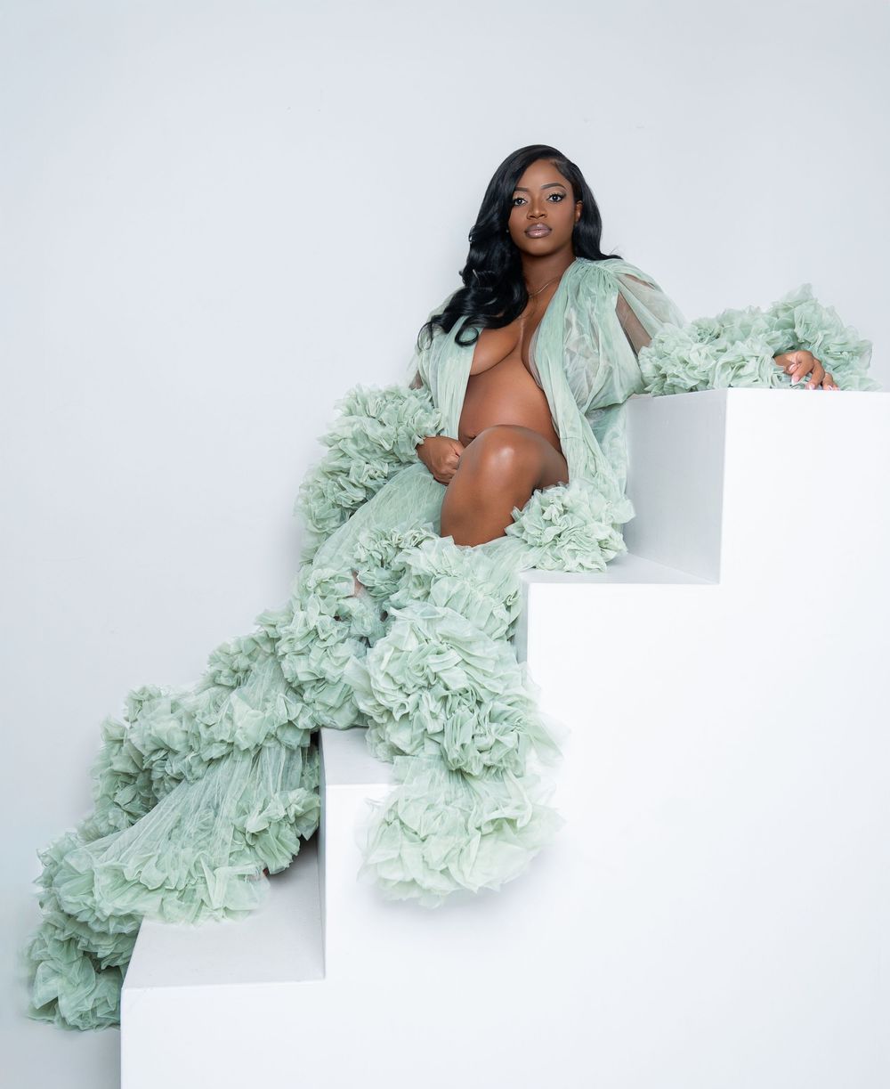 Pregnant woman in elegant sage green ruffled tulle maternity gown posing gracefully on white geometric steps.