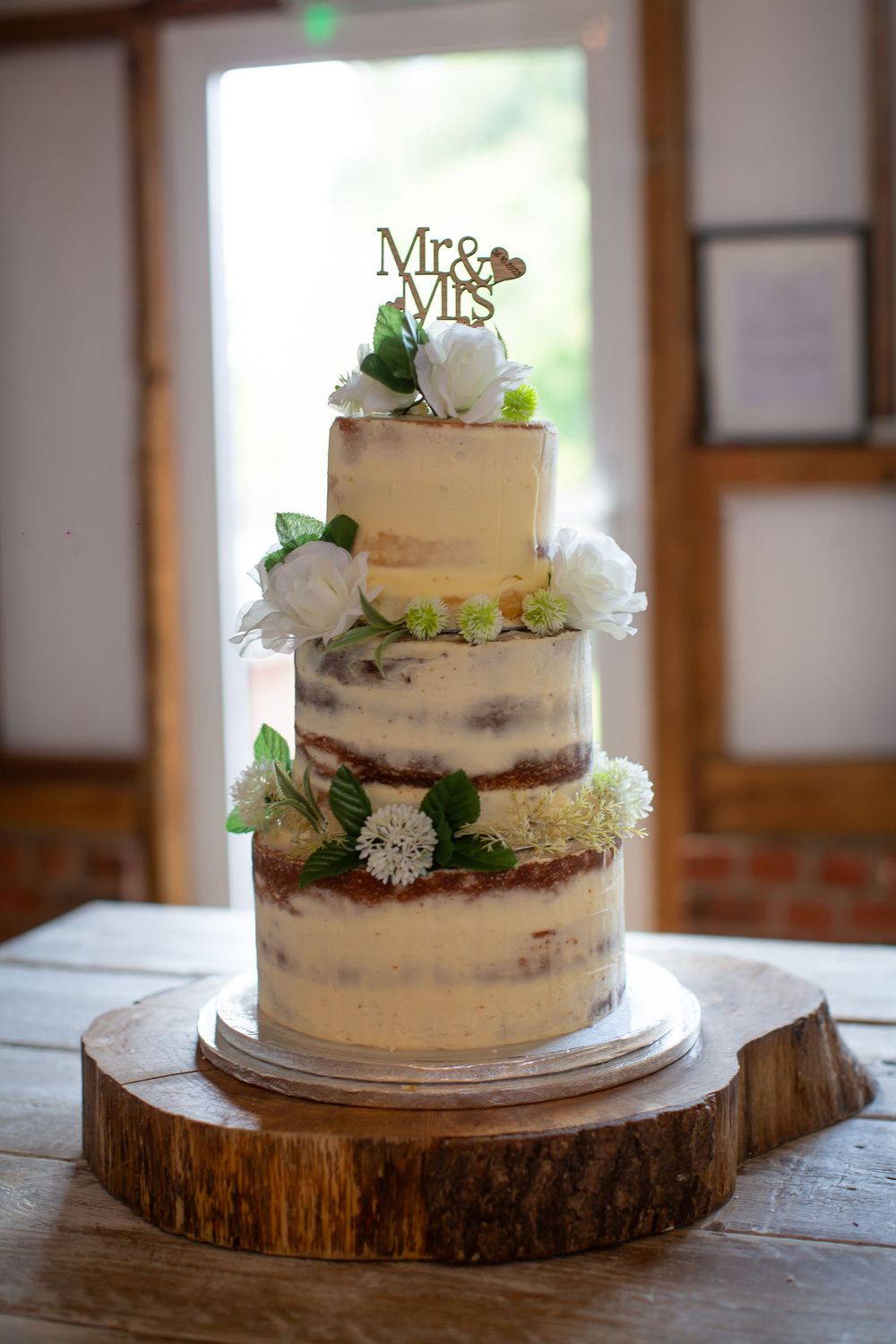 Rustic naked wedding cake decorated with white flowers on a wooden slice.