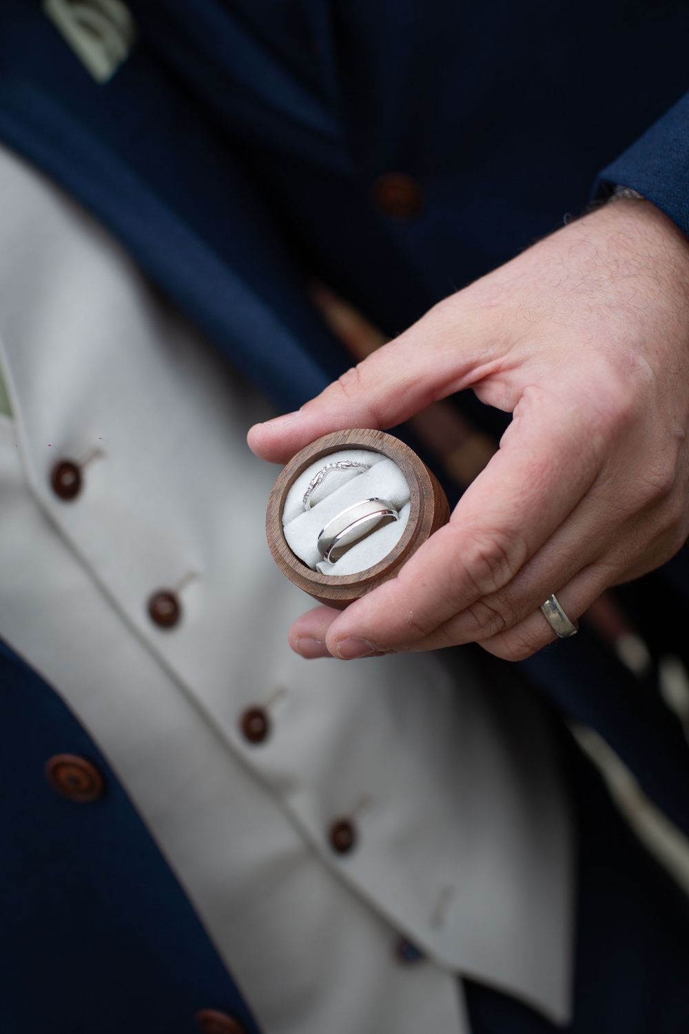Close-up shots of wedding rings being held against navy blue formal attire.