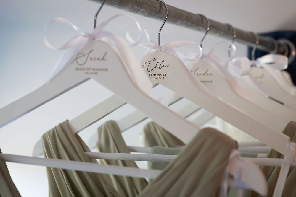 Wedding dress hangers with personalized name tags lined up in soft lighting.