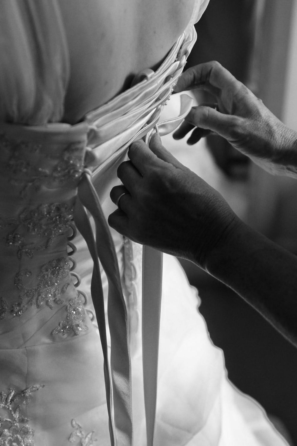 Close-up shots of hands adjusting intricate details on a white wedding dress.