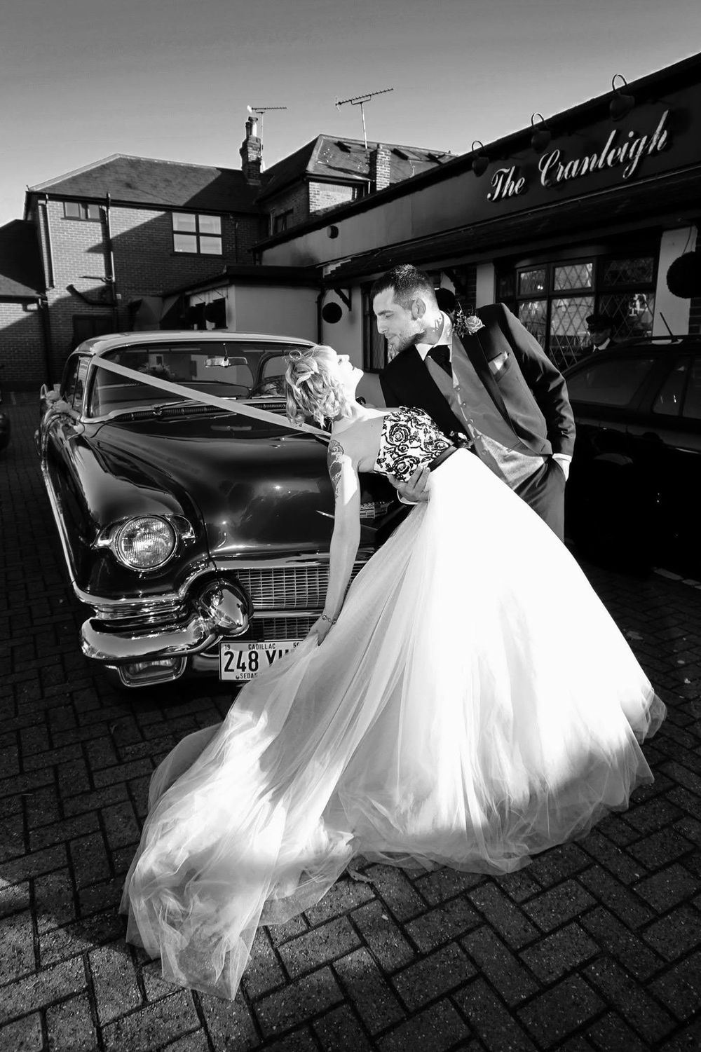 Classic vintage car with flowing white wedding dress visible against cobblestone pavement.