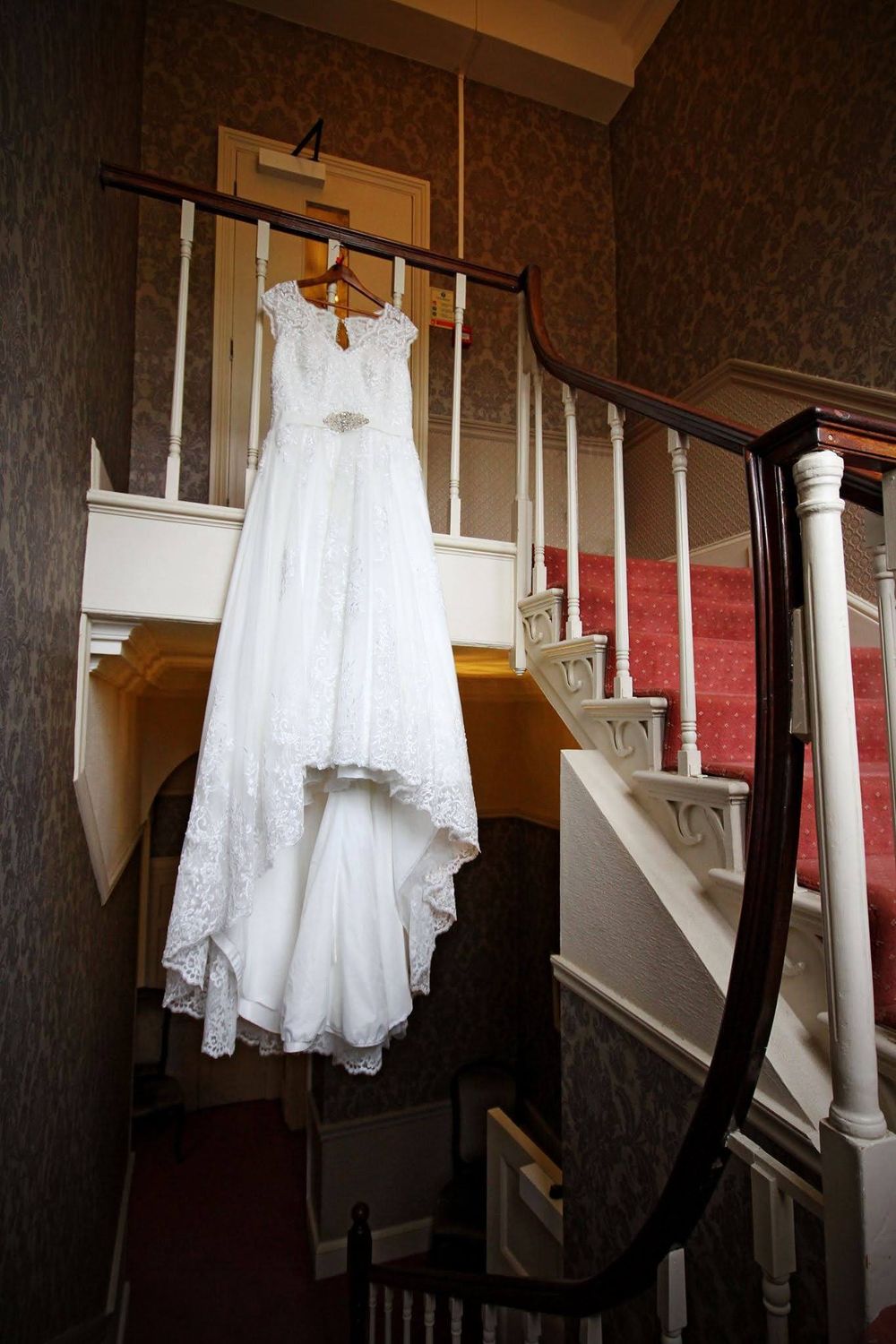 Wedding dress displayed hanging on staircase with dramatic lighting and shadows.