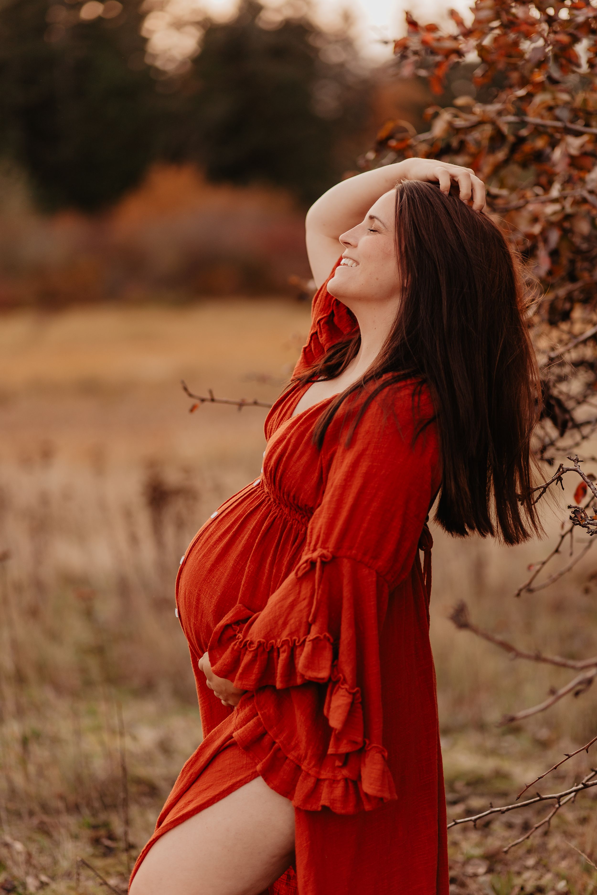 A woman in a flowing red dress poses expressively against an autumn backdrop with brown foliage.