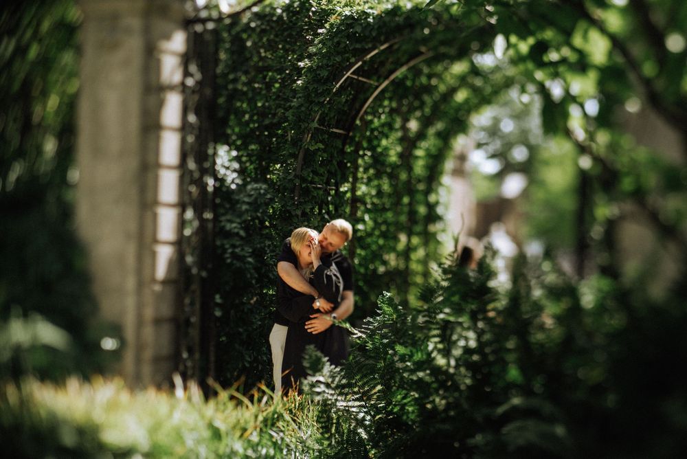 Couple embracing in a lush green garden setting with natural sunlight filtering through.