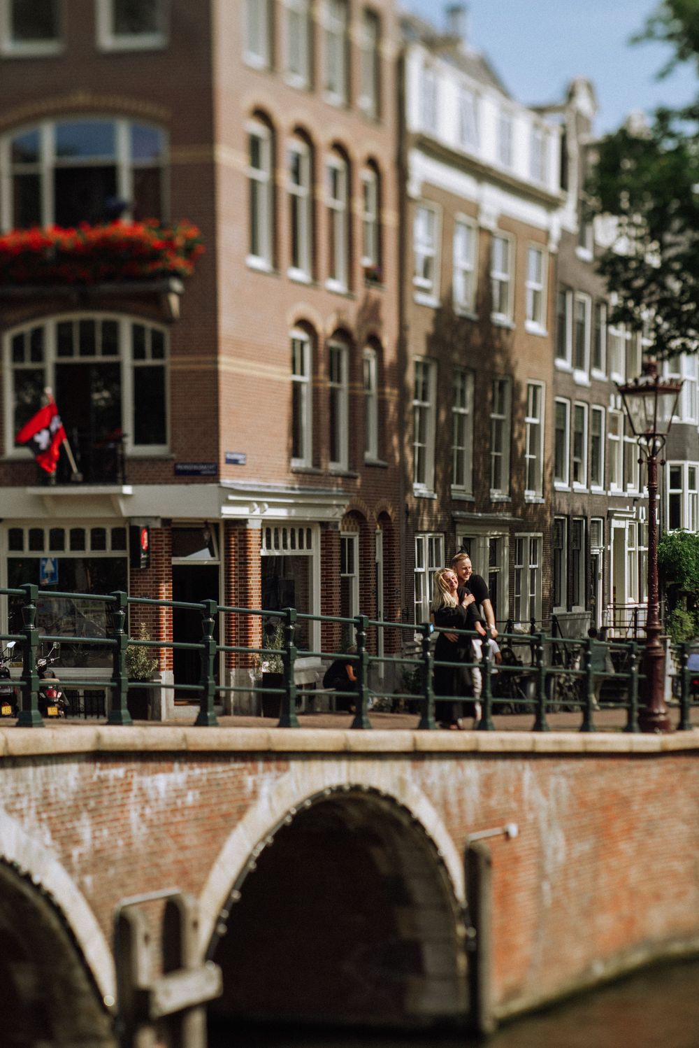 Scenic Amsterdam canal with brick bridge and traditional Dutch architecture in warm sunlight.