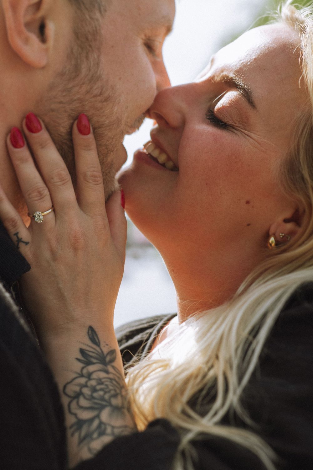 Close-up of a tender romantic moment showing hands with red nail polish and floral tattoo.