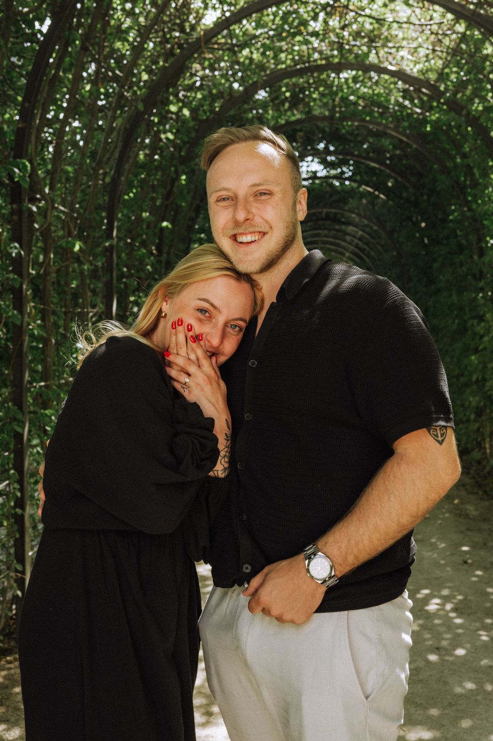 Happy couple in black and white outfits embracing in a sunlit garden setting.