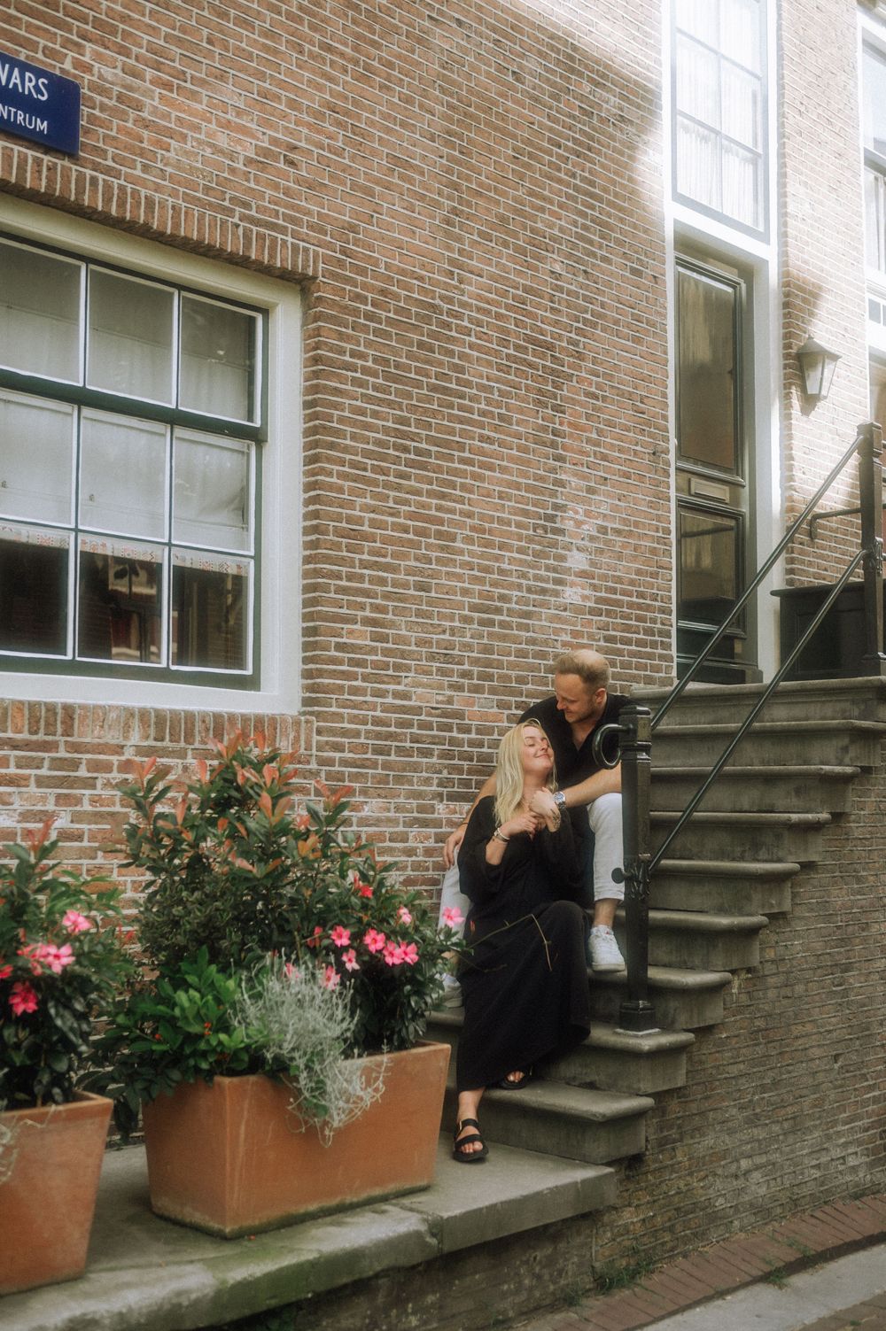 Couple sharing a sweet moment on brick building steps with potted flowers.
