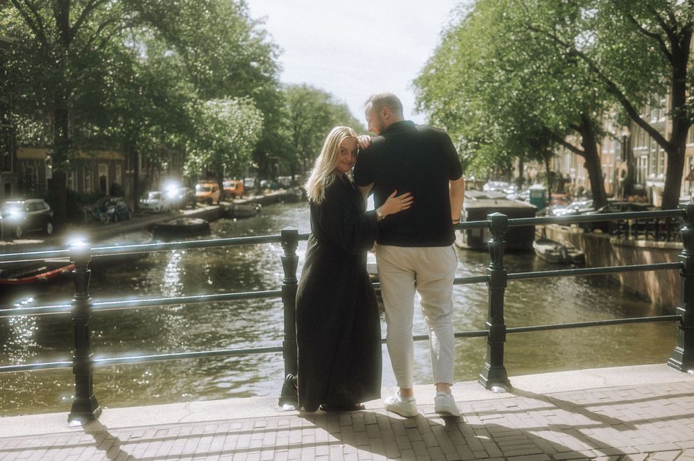 Couple overlooking Amsterdam canal while standing on bridge.