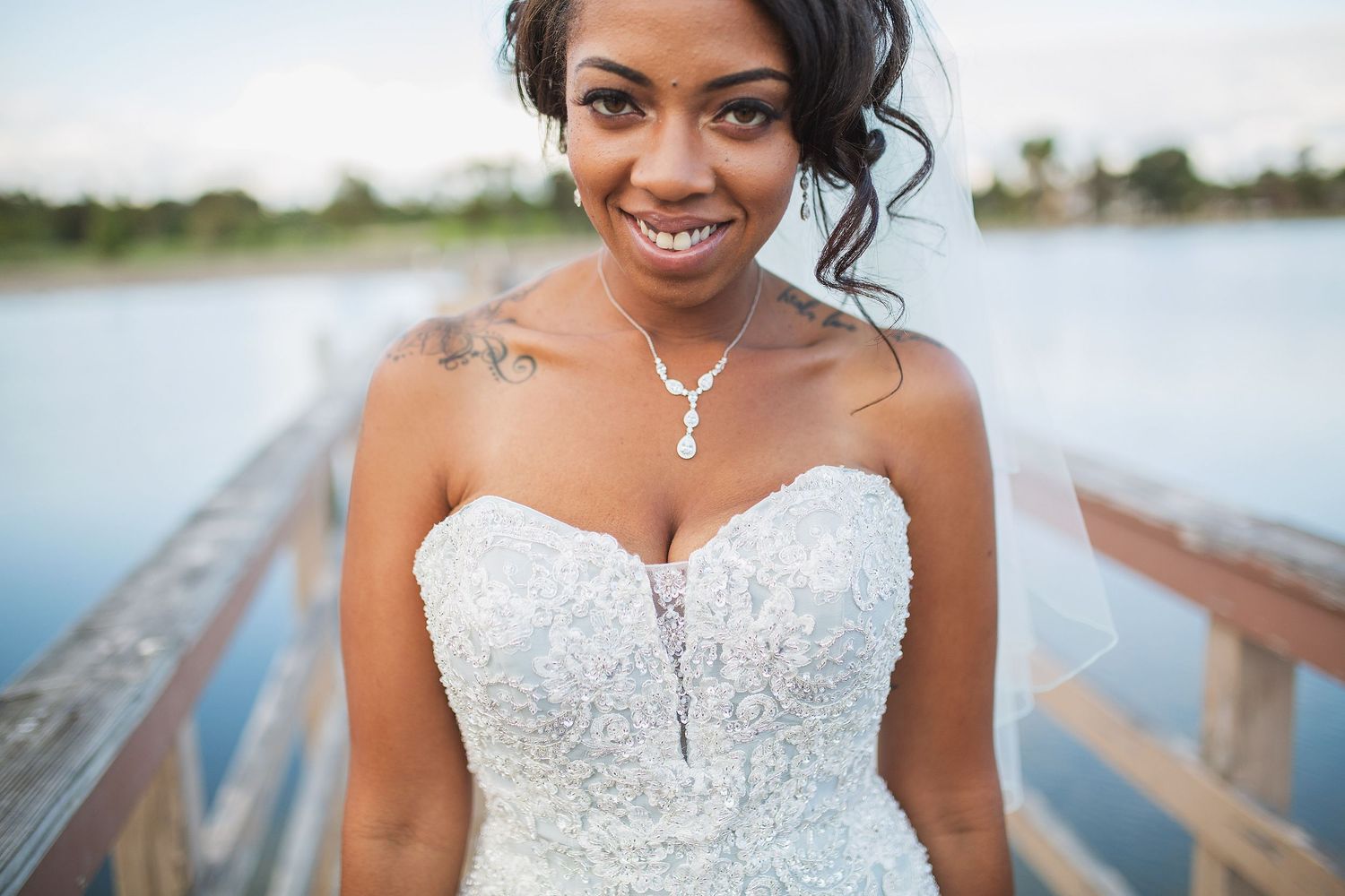 Beautiful bride in a beaded white wedding gown poses against a lakeside backdrop.