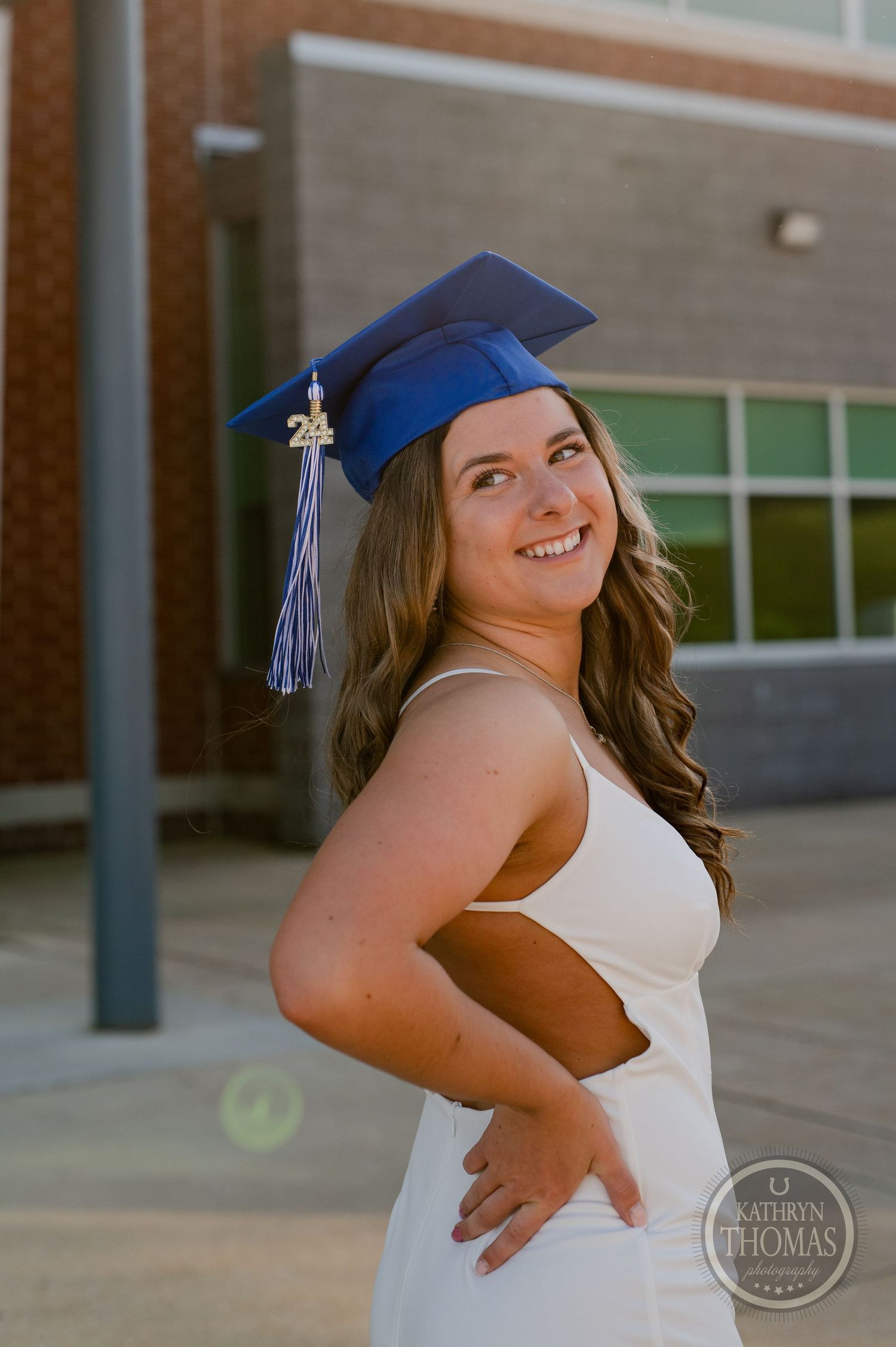 Graduate wearing blue cap with tassel smiles in white dress during outdoor photo session.