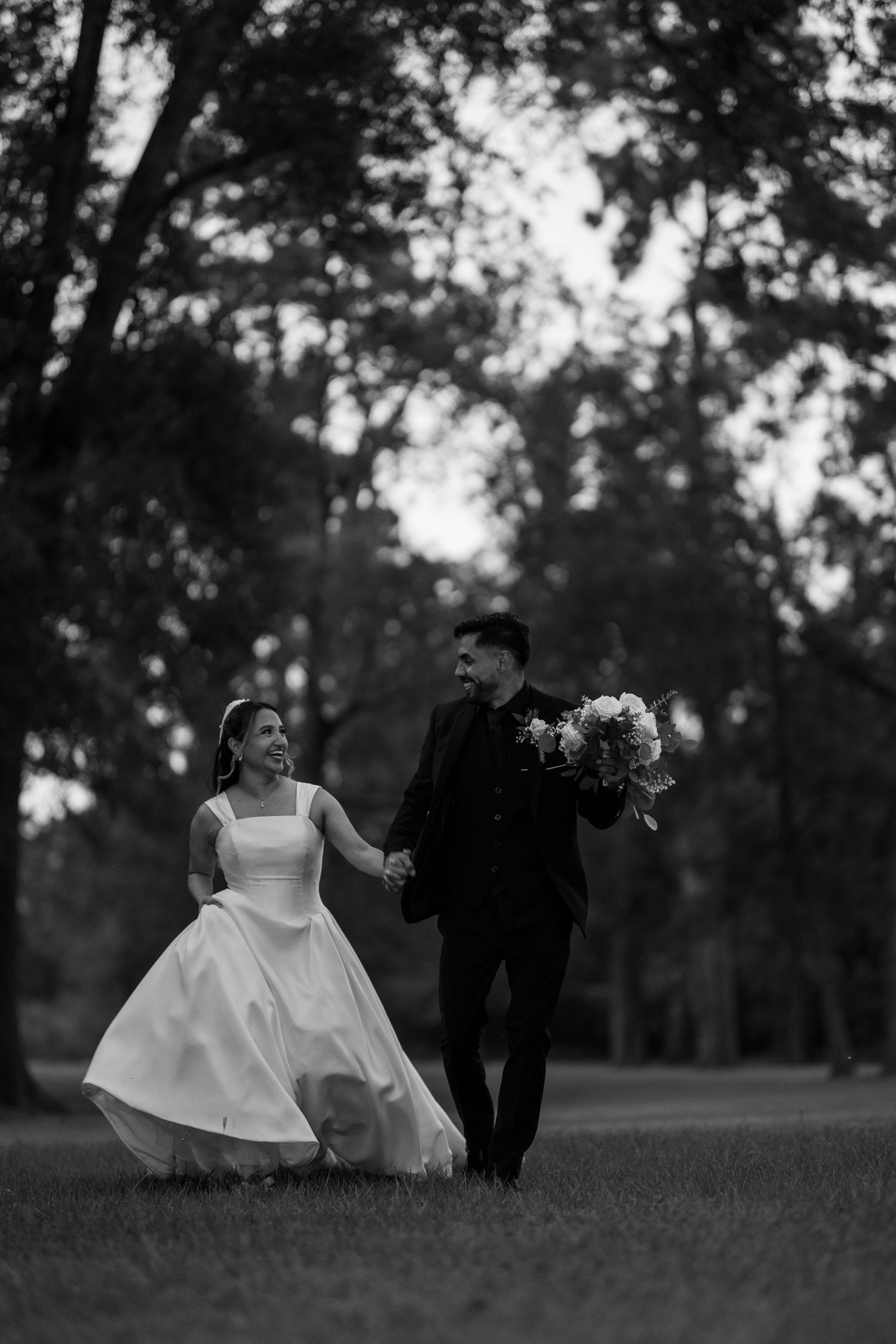 A black and white wedding photo capturing movement across a serene outdoor landscape.
