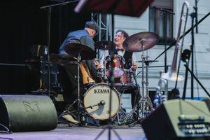 Musicians playing drums and bass perform energetically at outdoor concert venue.