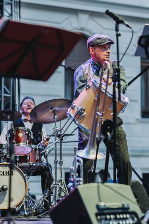 Jazz musicians perform on outdoor stage with drummer and bassist visible.