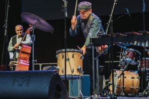 Jazz ensemble performs on outdoor stage with drummer and bassist visible.