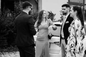 Wedding guests mingling and chatting outside near a parked car.