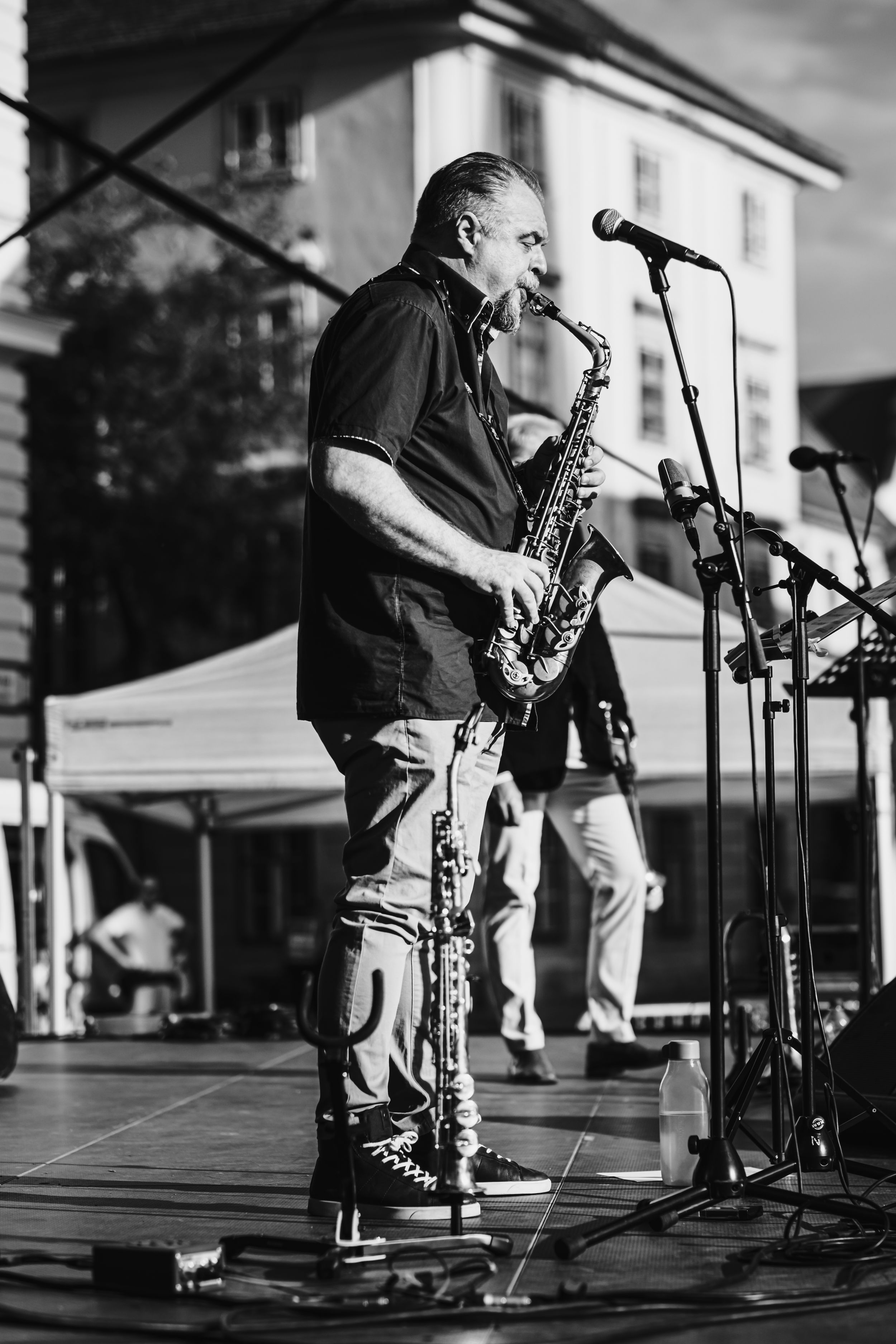 Black and white photo of a saxophone player performing on stage with microphones and musical equipment.