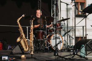 A drummer sits behind a Premier drum kit on stage during a live performance.