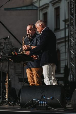 A saxophone player and another musician perform together on stage at an outdoor venue.