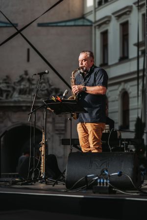 Saxophone performer plays solo on an outdoor stage with historic architecture in background.