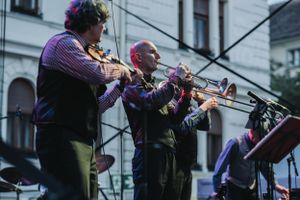 Three trumpet players performing together in colorful uniforms at an outdoor concert.