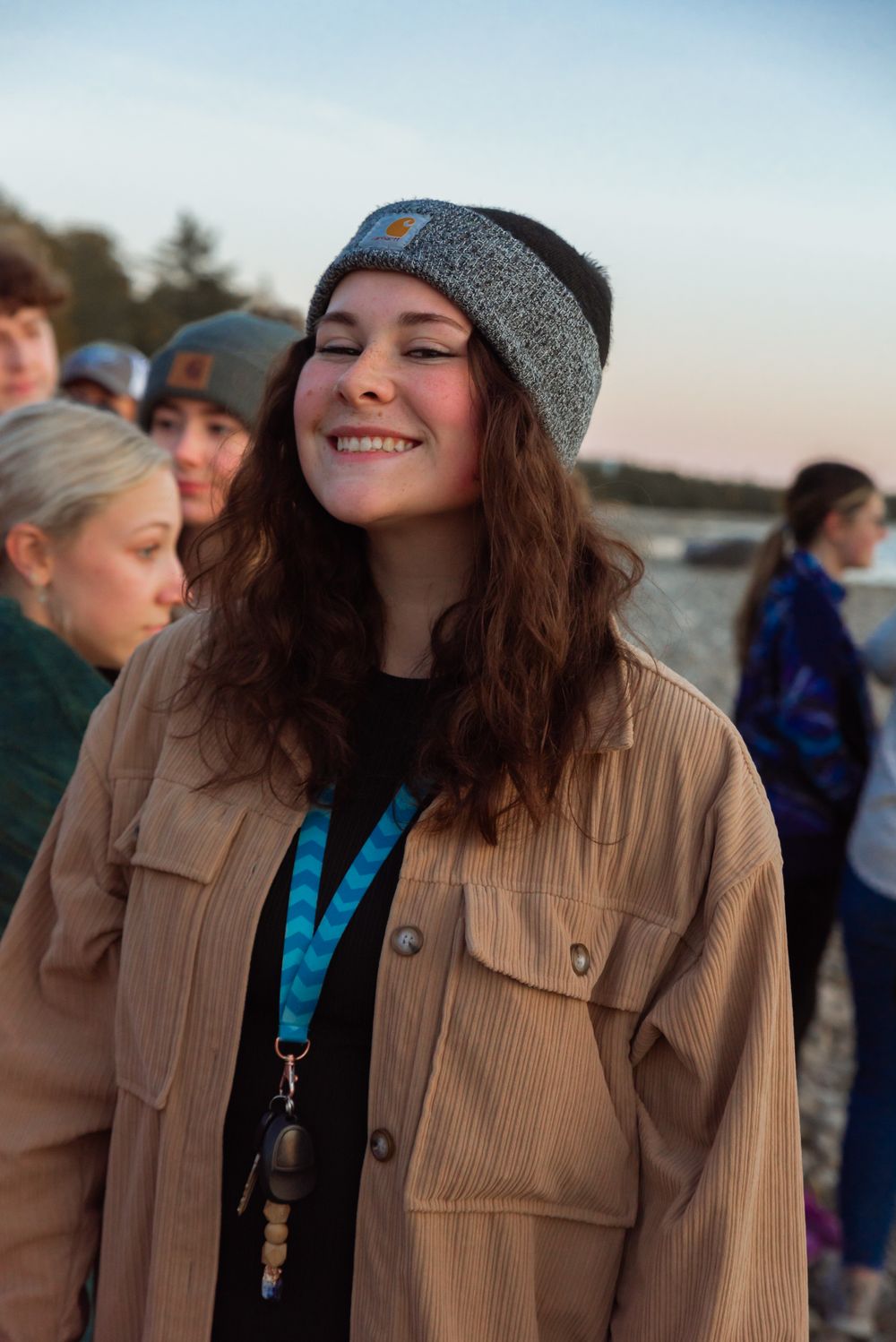 A person in a beanie and corduroy jacket smiles with eyes closed during golden hour at the beach.