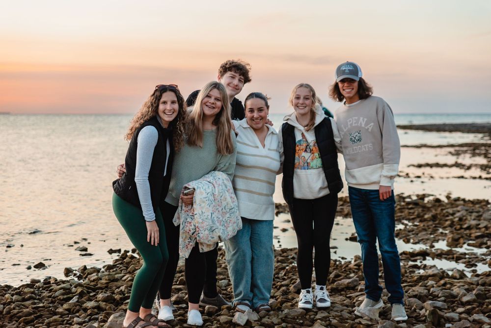 Group of friends enjoying sunset together on rocky beach shore.