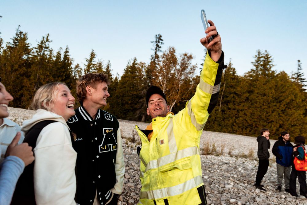 Friends taking selfie outdoors with evergreen trees in background.