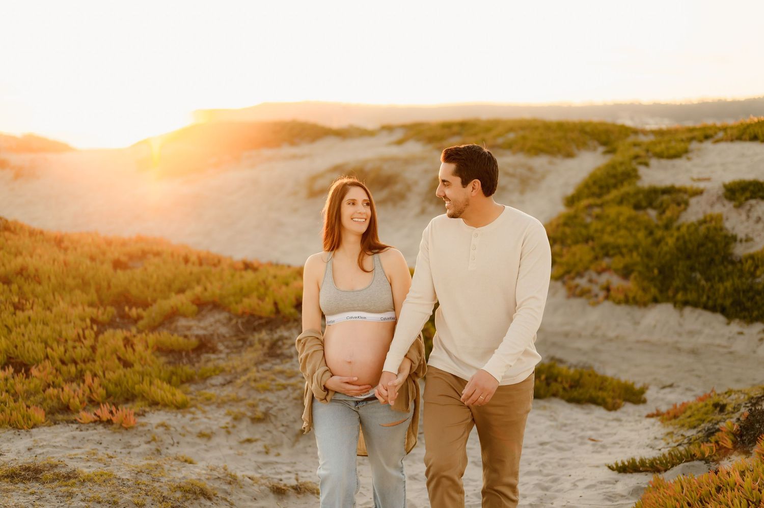 jeans and sports bra maternity photoshoot Carpinteria, of couple walking in sand dunes, by Camarillo photographer