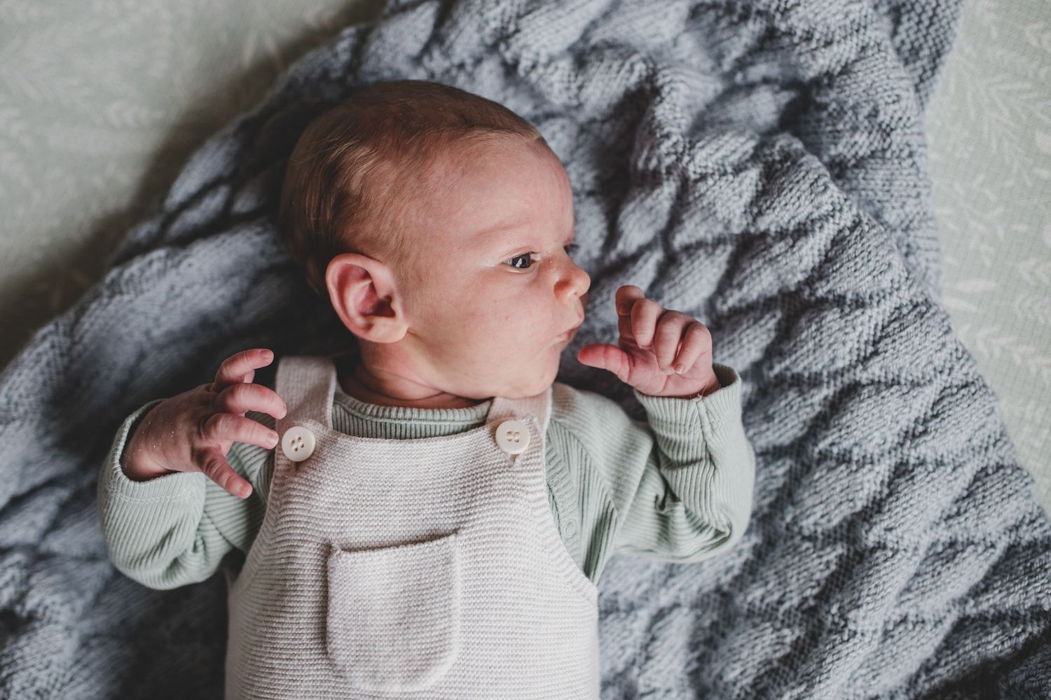 A peaceful newborn baby in a white onesie rests on a soft gray knit blanket.
At home Newborn photography, Suffolk.