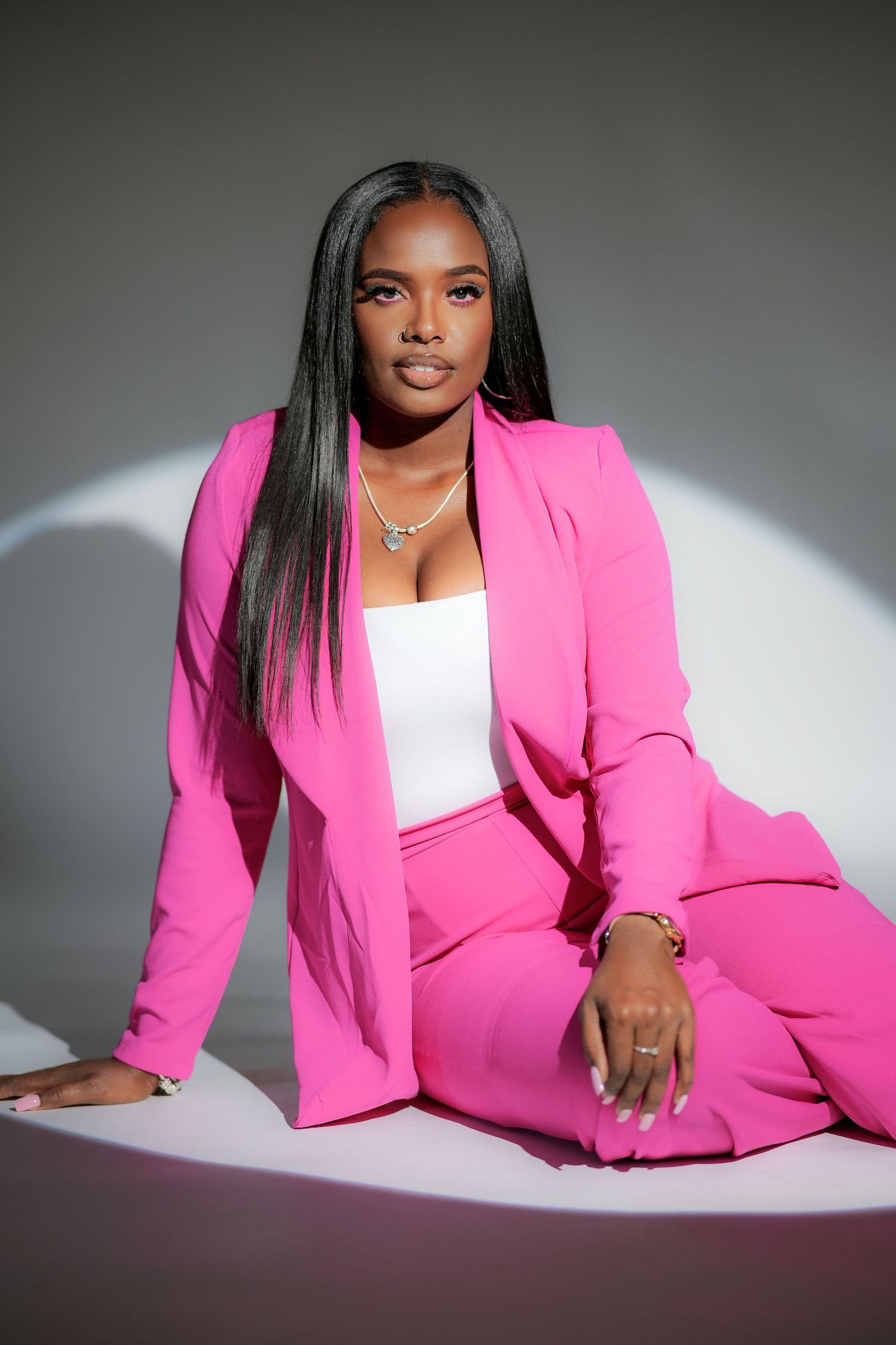 A model in a vibrant hot pink business suit and white top poses elegantly against a gray backdrop.