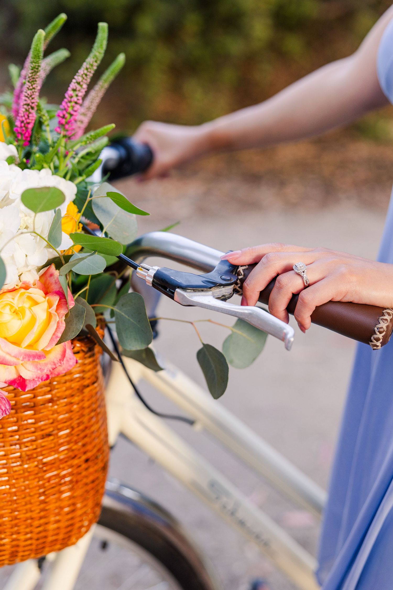 Close-up of hands holding bicycle handlebars with floral basket arrangement.