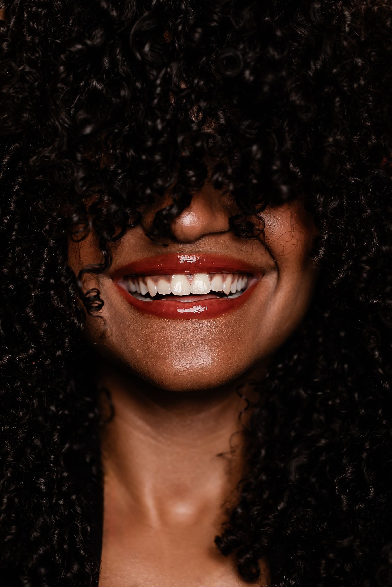 Close-up photo of a bright smile framed by natural curly hair against dark background.