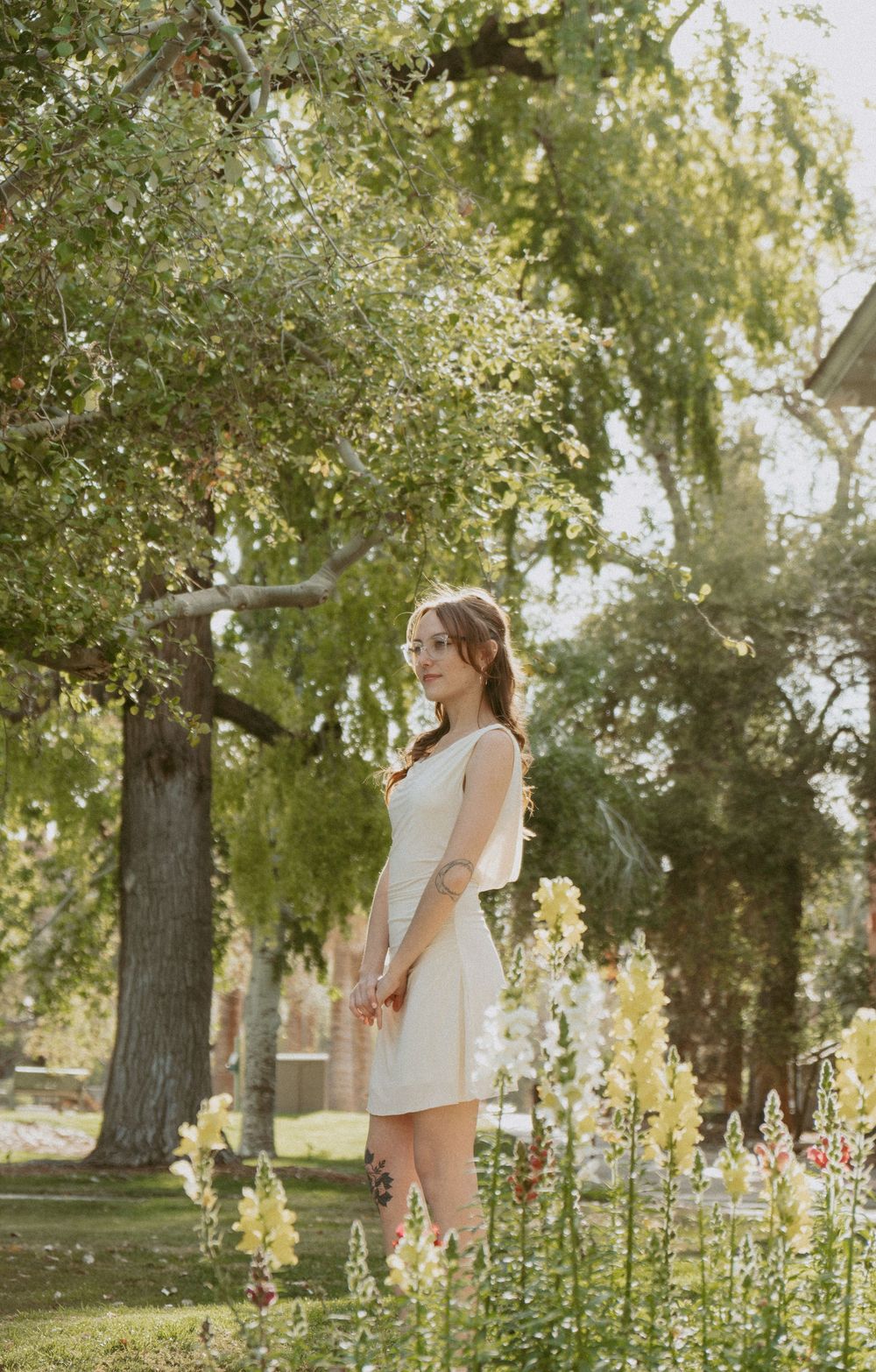 White dress and floral garden scene captured in dreamy natural light with tall trees in the background.