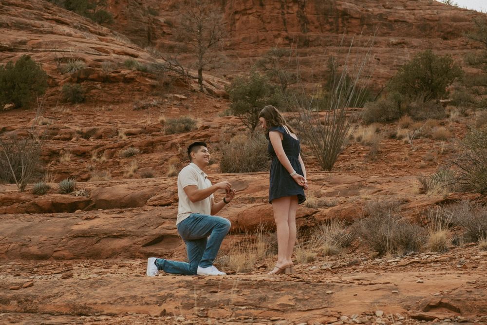 A proposal moment captured against red rock formations in a desert landscape with desert plants and sand.