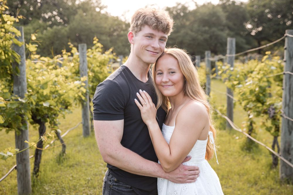 A romantic couple embrace in a sun-lit vineyard with lush green grapevines creating a beautiful backdrop.