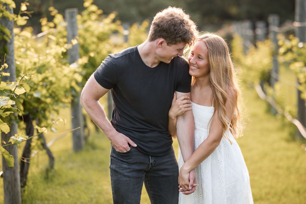 A couple shares an intimate moment while holding hands in a sunlit vineyard among golden foliage in late afternoon.