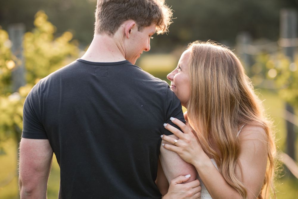A romantic couple embraces outdoors during golden hour with sunlit trees in the background.