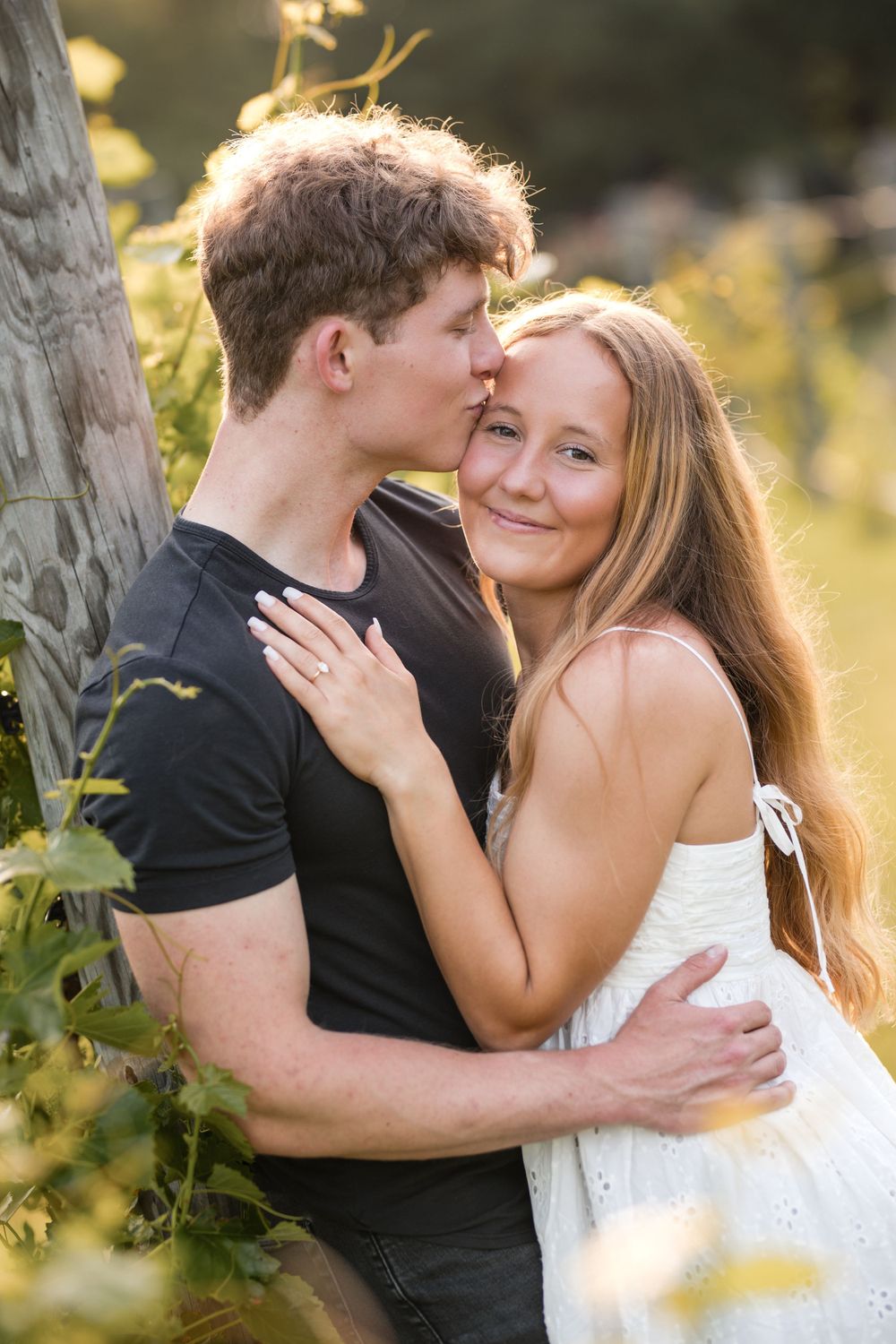 Romantic couple embracing in nature with golden sunlight filtering through trees as they share an intimate moment.