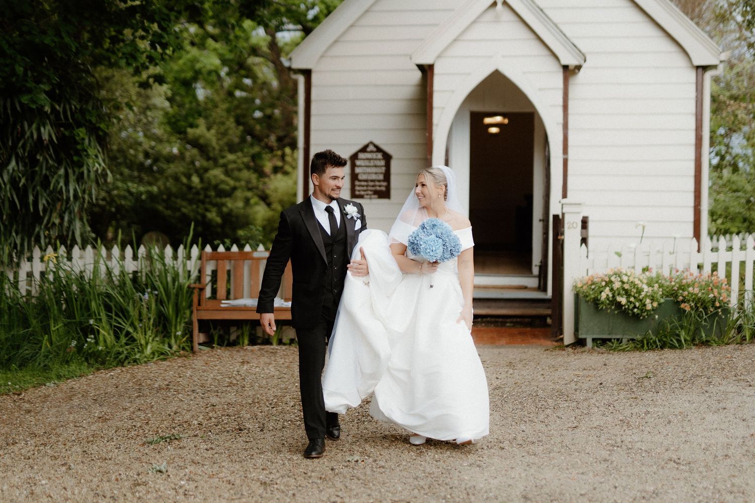 Couple exits small white chapel after wedding ceremony.