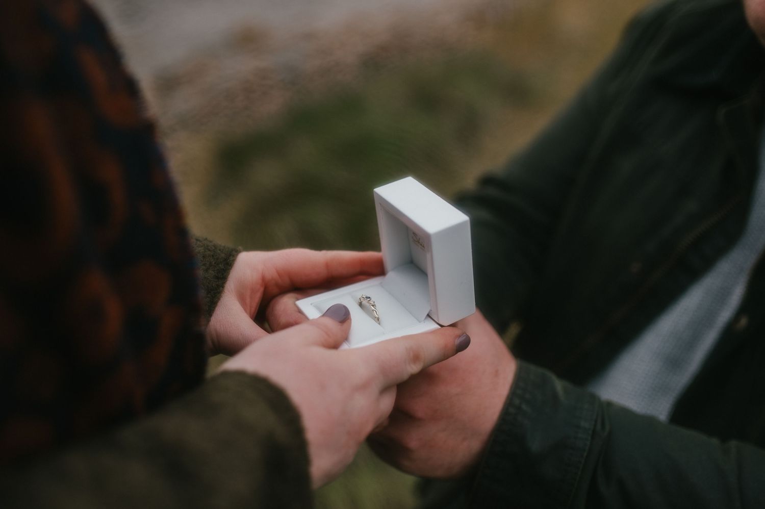 Someone holding and presenting an engagement ring box during a special moment outdoors.