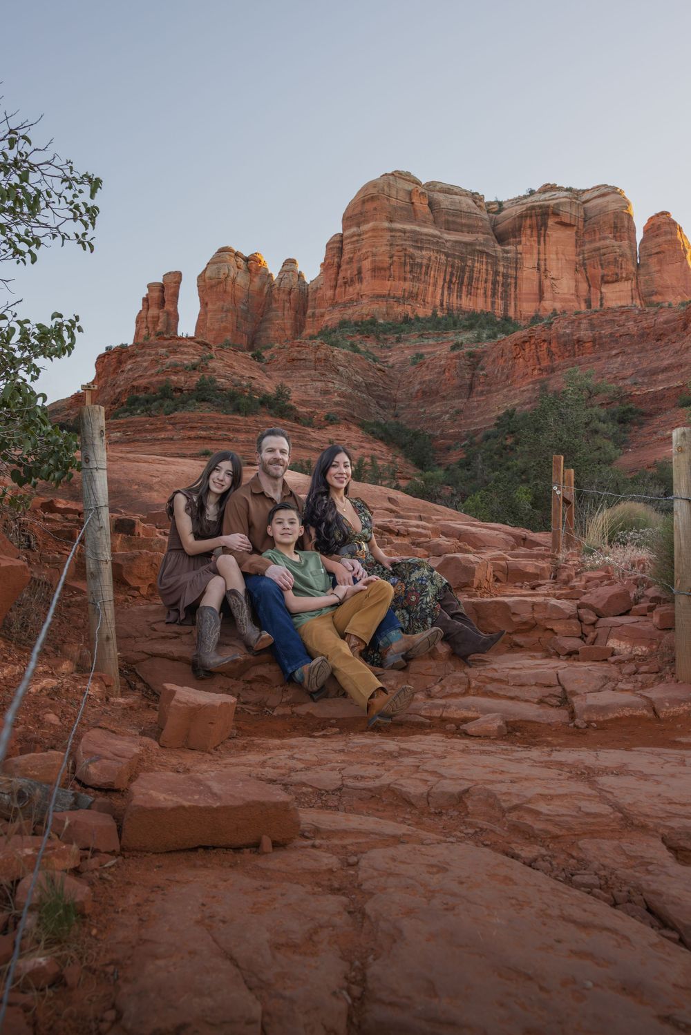 Family sitting together on red rock steps with Cathedral Rock formation in Sedona background.
