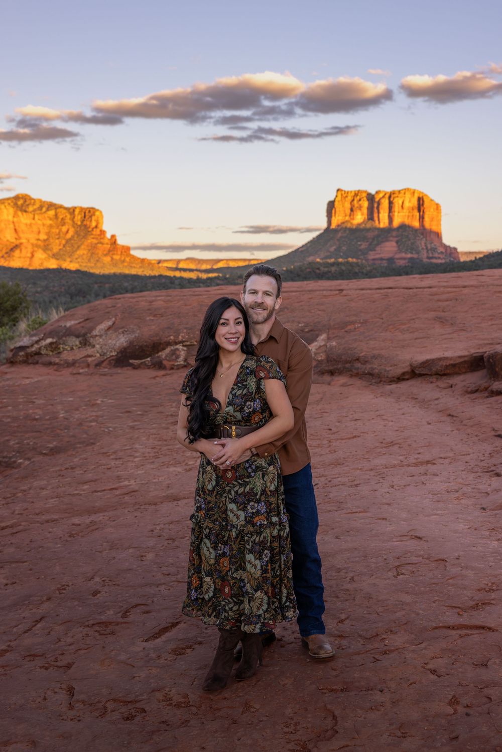 Couple embracing at sunset with Sedona red rock buttes glowing golden in the background.