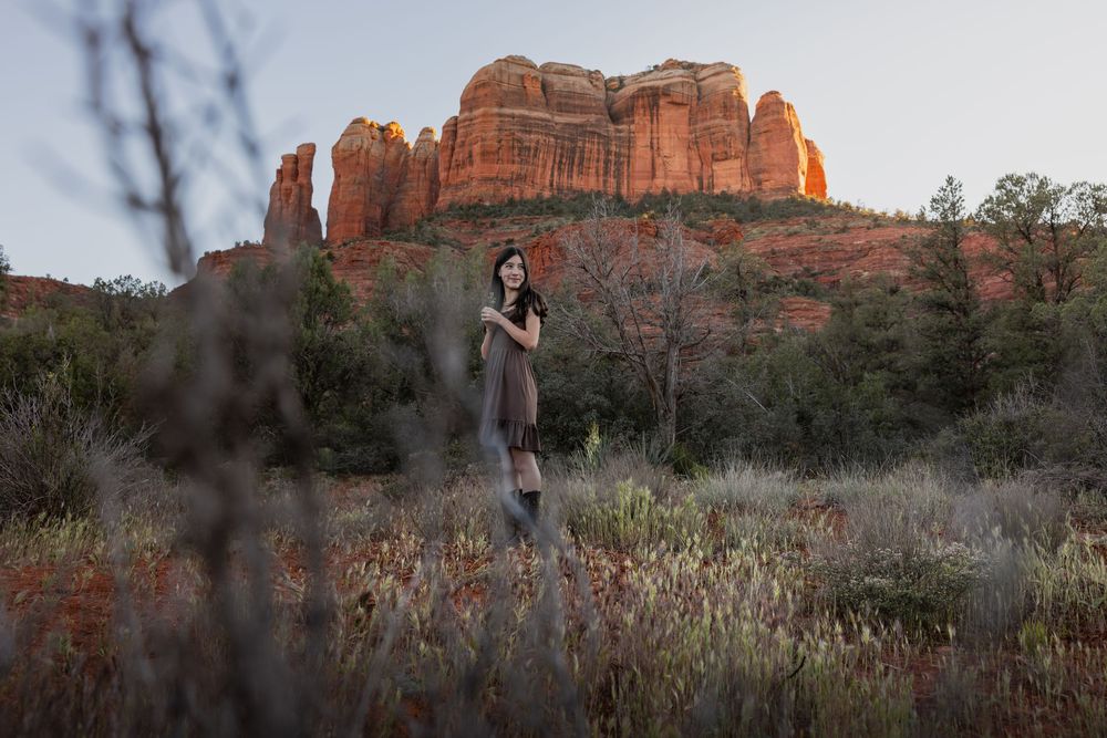 Young woman standing in a field with iconic Sedona red rock formations glowing at sunset.